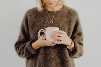 A woman in a brown sweater holds a pink, minimalist mug
