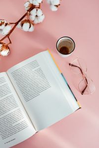 An open book, coffee, glasses and a cotton branch on a pink background