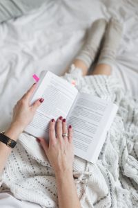 Soft photo of woman on the bed with the book and cup of coffee in hands