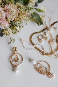 Gold jewellery on white marble - necklace, bracelets, earrings, flowers