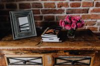 Photo frame, books and pink flowers in a vase on a wooden commode