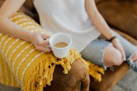 Kaboompics - Woman with a cup of coffee & book, yellow blanket, blue jeans pants