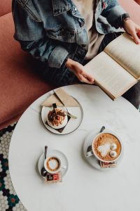 Kaboompics - A woman eats meringue, drinks coffee and reads a book in a patisserie