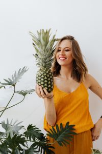 A beautiful smiling young woman is holding a pineapple