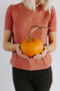 Women's hands in sweater are holding pumpkin