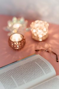 An open book, candles and glasses on a pink background