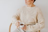 A woman in a warm sweater drinks tea