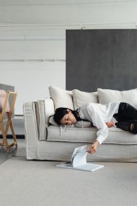 A young Asian woman lies on the couch and reads a book