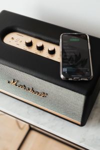 Black speaker on marble table, white wall, mobile phone