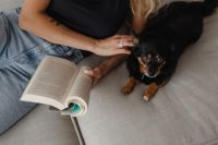 Kaboompics - A woman reads a book on the couch with her dog