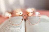 An open book, glasses and a cotton branch on a pink background