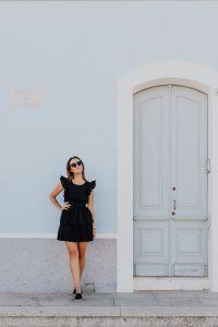 Kaboompics - A young woman with dark hair wearing a black dress poses by the blue building
