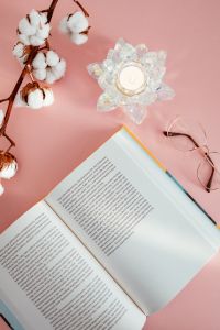 An open book, candle, glasses and a cotton branch on a pink background
