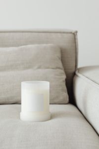 Candle in white glass with label on linen couch