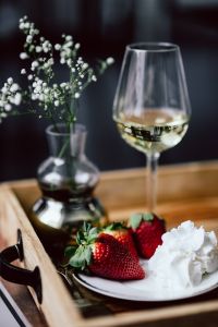 Strawberries with cream and glass of white wine on wooden tray