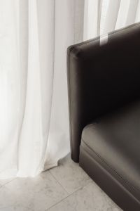 Detail of a black leather armchair with marble flooring and white curtains