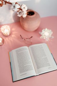 An open book, candles, cotton branch and glasses on a pink background