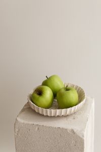 Kaboompics - Three Green Apples in a White Fluted Bowl on Stone Pedestal, Vertical Still Life with Copy Space