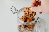Kaboompics - Hand Reaching for a Chocolate Chip Cookie in a Glass Jar at Home
