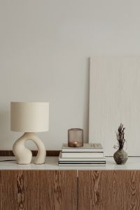 Kaboompics - Ceramic Lamp with Dried Vase, Candle and Books Against Textured Wall Panels