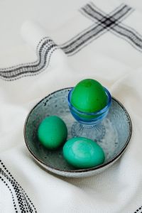 Kaboompics - Green Easter Egg in a Blue Glass Egg Cup with Painted Eggs in a Bowl