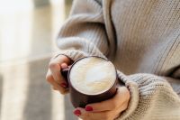 Kaboompics - Close-Up of Cappuccino Foam in a Brown Mug, Hands Wrapped in a Cream Knit Sweater