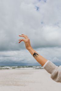 Kaboompics - Swallow Tattooed Hand Reaching Above a Sandy Shore, Coastal Lifestyle and Travel Background