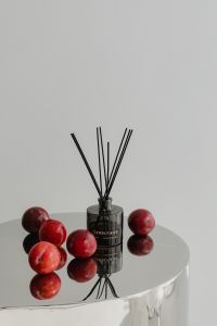 Kaboompics - Black Reed Diffuser with Red Plums on Reflective Chrome Table