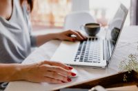 Kaboompics - Woman Using a Laptop and Wireless Mouse on White Bedding with Coffee and Baby’s Breath Flowers