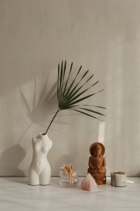 Kaboompics - White Torso Vase With Palm Leaf, Wooden Buddha, Matchsticks, and Rose Quartz