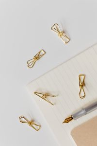 Kaboompics - Macro Silver Fountain Pen Nib with Scattered Gold Paper Clips on Lined Writing Paper