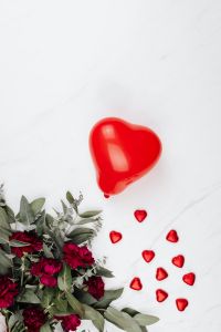 Kaboompics - Red Heart Balloon and Heart-Shaped Pralines beside Burgundy Flowers on White Marble, Valentine's Day Still Life