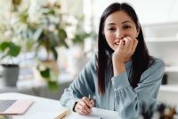 Kaboompics - Smiling Asian Woman Writing Notes at Her Desk