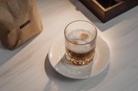 Kaboompics - Foamy Layered Coffee in a Clear Glass on White Saucer, Home Coffee Bar Still Life