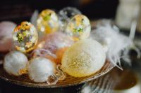 Kaboompics - Pastel Glass Easter Eggs and White Feathers in a Gold-Patterned Decorative Basket