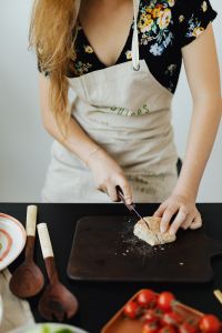 Kaboompics - Hands Slicing Bread on a Cutting Board in a Floral Apron
