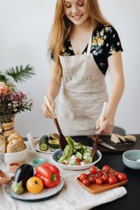 Kaboompics - Smiling Home Cook Tossing Salad beside Bread and Colorful Produce