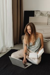 Kaboompics - Woman Using a Laptop While Holding an Open Book at Home