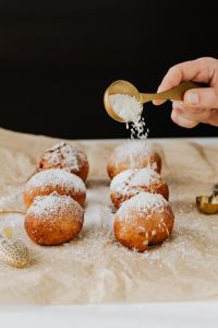 Kaboompics - Hand Shaking Powdered Sugar from a Gold Sifter over Polish Paczki, Dark Backdrop
