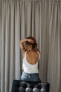 Kaboompics - Back View of Woman in White Tank Top and Jeans by Neutral Curtains