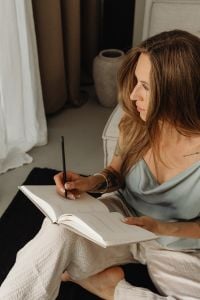 Kaboompics - Woman Journaling on a Sofa Beside Neutral Curtains