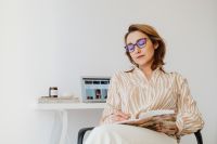 Kaboompics - Woman Reading a Floral Notebook beside Laptop at Home Desk