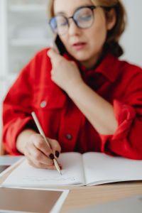 Kaboompics - Woman in Glasses Writing in a Notebook during a Phone Call beside Her Laptop