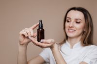 Kaboompics - Smiling Esthetician Presenting Amber Oil Dropper, Natural Skincare Campaign Portrait