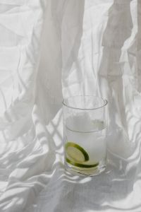 Kaboompics - Tall Glass of Lime-Infused Water on Draped White Linen with Soft Window Shadows