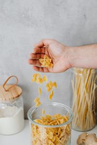 Kaboompics - Hand Adding Farfalle Pasta to a Glass Food Storage Jar in a Home Kitchen