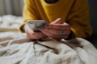 Kaboompics - Close-Up of Hands Using Smartphone on White Bedding, Cozy Home Lifestyle