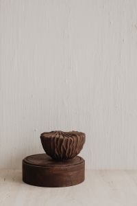 Kaboompics - Sculptural Brown Ceramic Vase on Round Wooden Pedestal Against Textured White Wall
