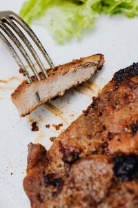 Kaboompics - Fork Holding a Bite of Grilled Pork Neck beside Charred Steak, Macro Food Photography