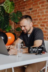 Kaboompics - Smiling Photographer Working with Laptop, Camera and Halloween Balloons